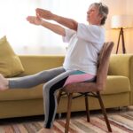 An elder woman practicing chair yoga at home